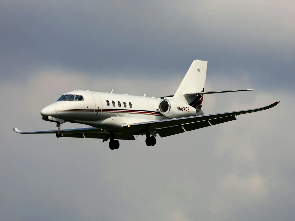 A white business jet climbing against a pale sky